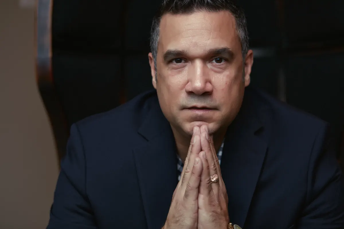 Ted Canto in a navy jacket, seated and listening thoughtfully
